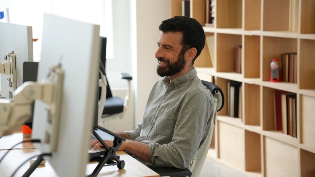A Gumlooper smiling at his desk by the office bookshelves